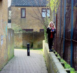 woman in black jacket standing on gray concrete pathway near brown brick building during daytime