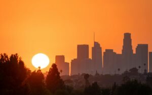 Bright orange sunset over downtown Los Angeles skyline with palm trees silhouetted.