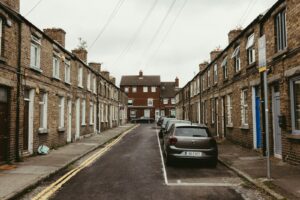 Narrow street lined with traditional terraced houses and parked cars.