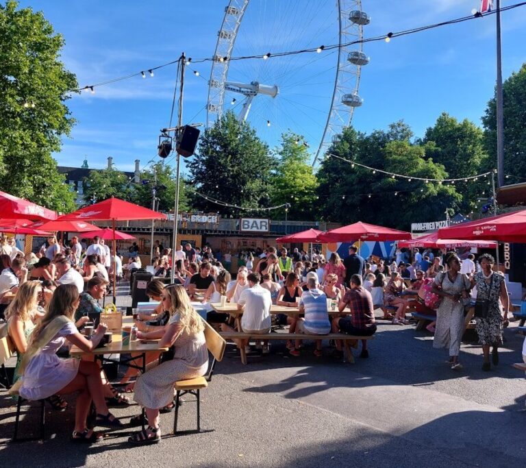 a group of people sitting at tables in front of a ferris wheel