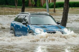 A blue car driving through a flooded street
